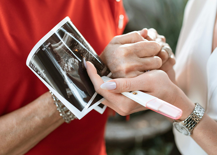 Two people holding a sonogram and pregnancy test, discussing a gift that feels creepy and invasive. Two people holding a sonogram and pregnancy test, discussing a gift that feels creepy and invasive.