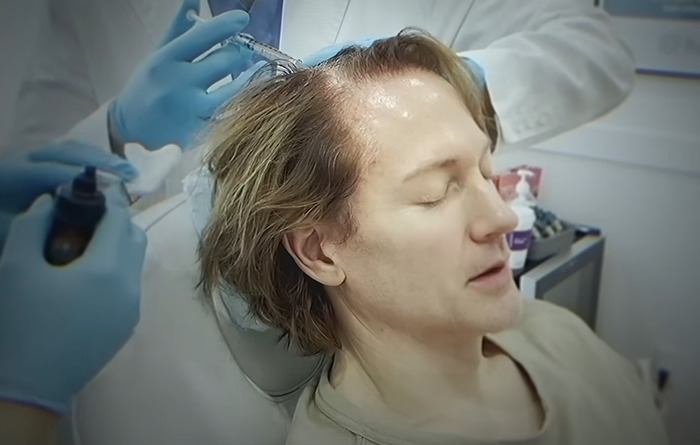 Bryan Johnson receiving longevity medication treatment, seated in a clinic, doctor in white coat and gloves applying injections. Bryan Johnson receiving longevity medication treatment, seated in a clinic, doctor in white coat and gloves applying injections.