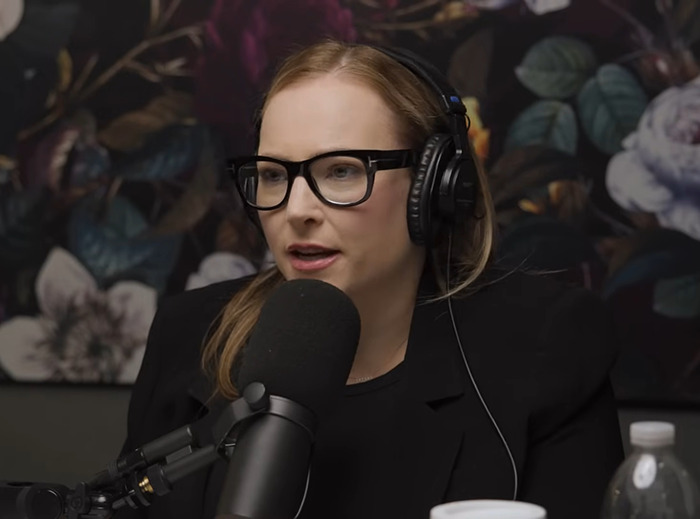 Meghan McCain with glasses and headphones speaking into a microphone, floral background. Meghan McCain with glasses and headphones speaking into a microphone, floral background.