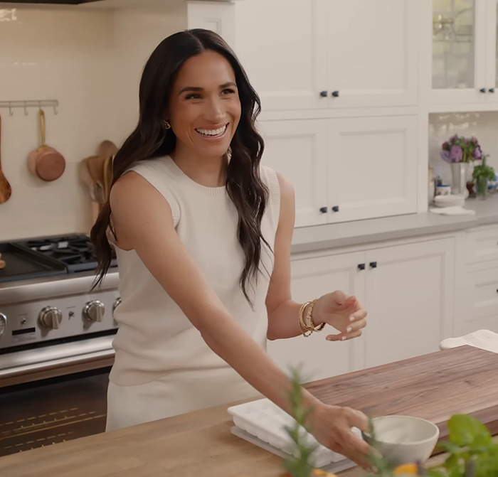 Meghan Markle smiling in a modern kitchen, reaching for a bowl on a countertop, embodying lifestyle themes. Meghan Markle smiling in a modern kitchen, reaching for a bowl on a countertop, embodying lifestyle themes.
