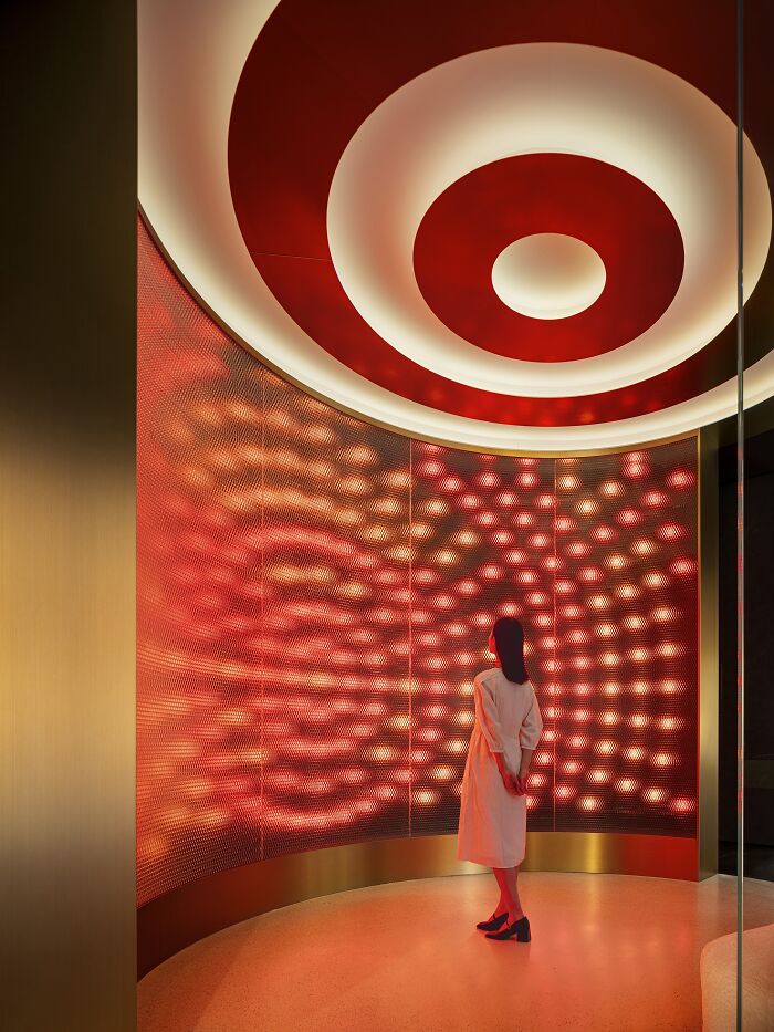 Woman in white dress admiring a red, circular light installation, showcasing excellence in interior design.