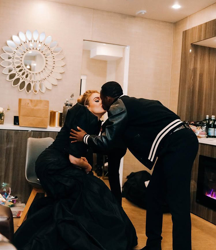 Adele in a long dress shares a kiss with Rich Paul in a jacket in a stylish living room. Adele in a long dress shares a kiss with Rich Paul in a jacket in a stylish living room.