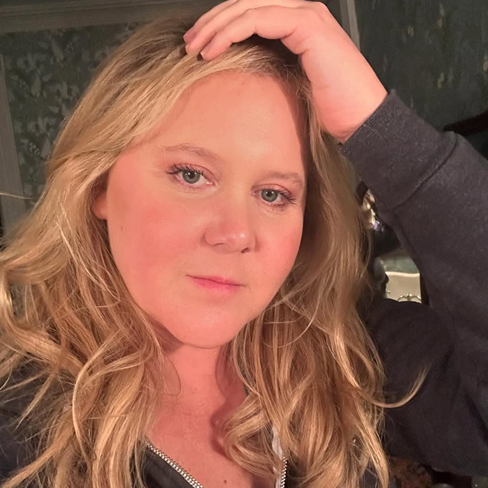 Amy Schumer wearing a dark hoodie in a softly lit room. Amy Schumer wearing a dark hoodie in a softly lit room.