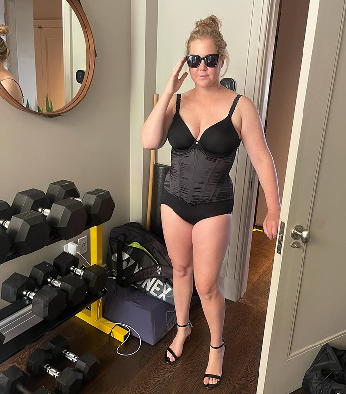 Amy Schumer in sunglasses wearing workout attire in a home gym setting. Amy Schumer in sunglasses wearing workout attire in a home gym setting.