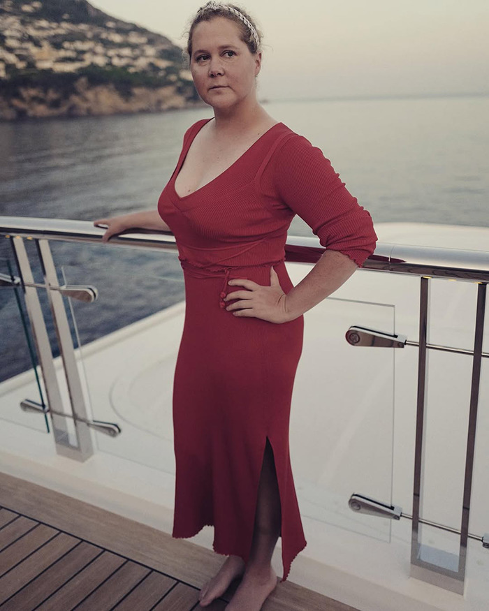 Amy Schumer in a red dress stands on a boat deck by the sea, looking thoughtful. Amy Schumer in a red dress stands on a boat deck by the sea, looking thoughtful.