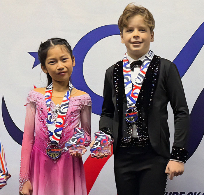 Child ice skating duo in costumes with medals, smiling after a performance. Child ice skating duo in costumes with medals, smiling after a performance.
