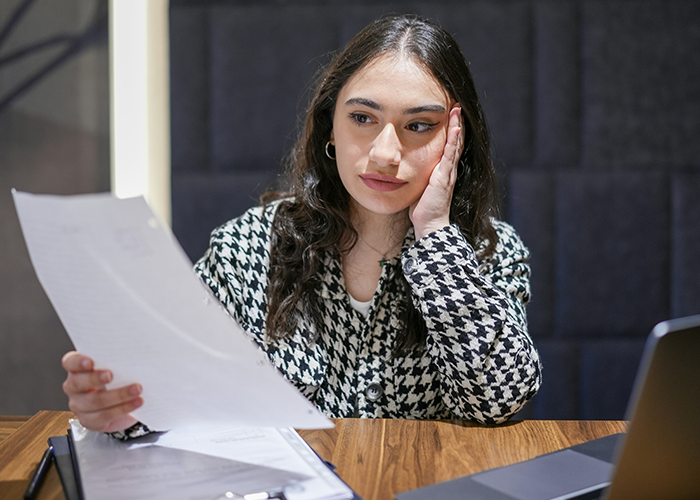 Woman contemplating two weeks' notice at a desk, holding a paper, looking stressed. Woman contemplating two weeks' notice at a desk, holding a paper, looking stressed.