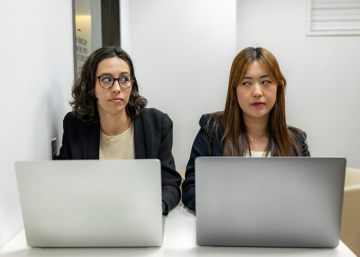 Two women sitting with laptops, one looking concerned; concept of giving notice at work discreetly. Two women sitting with laptops, one looking concerned; concept of giving notice at work discreetly.