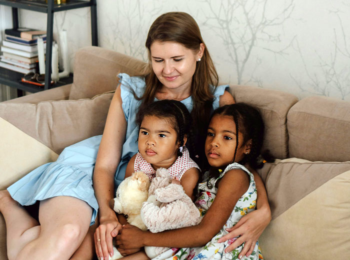 Babysitter with two children on a sofa, one holding stuffed animals, highlighting unexpected extra tasks. Babysitter with two children on a sofa, one holding stuffed animals, highlighting unexpected extra tasks.