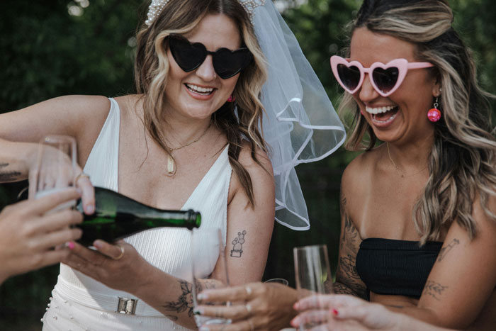 Brides at a bachelorette party laughing and pouring champagne, wearing heart-shaped sunglasses. Brides at a bachelorette party laughing and pouring champagne, wearing heart-shaped sunglasses.