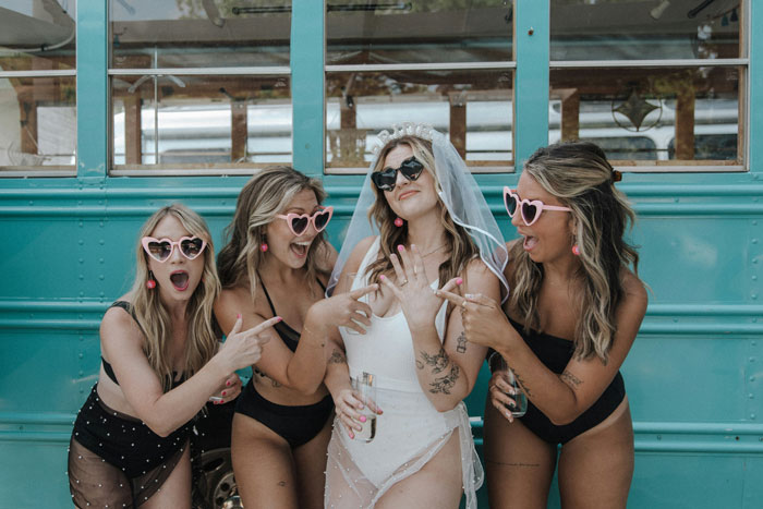 Women in swimsuits with heart-shaped sunglasses celebrate at a bachelorette party, posing playfully in front of a blue bus. Women in swimsuits with heart-shaped sunglasses celebrate at a bachelorette party, posing playfully in front of a blue bus.