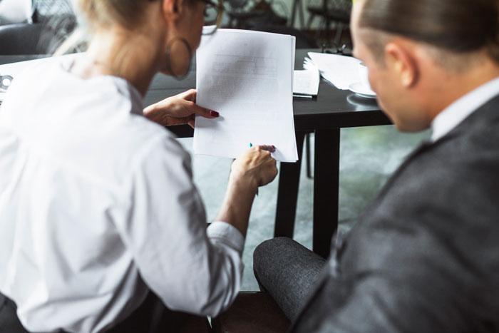 Two employees discussing a document related to bereavement and miscarriage policies in an office setting. Two employees discussing a document related to bereavement and miscarriage policies in an office setting.