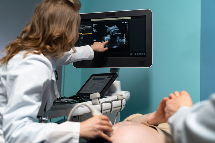 Doctor performing an ultrasound, displaying fetus image on screen, highlighting bereavement support in miscarriage cases. Doctor performing an ultrasound, displaying fetus image on screen, highlighting bereavement support in miscarriage cases.