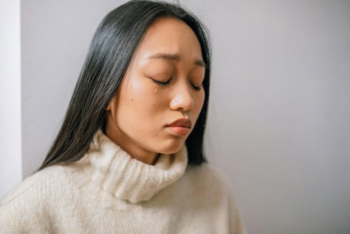 Woman in a cream sweater with teary eyes, contemplating work-life challenges and employment concerns. Woman in a cream sweater with teary eyes, contemplating work-life challenges and employment concerns.