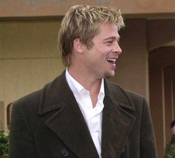 A smiling man in a dark coat stands outdoors, representing celebrity secrets and scandals discreetly.