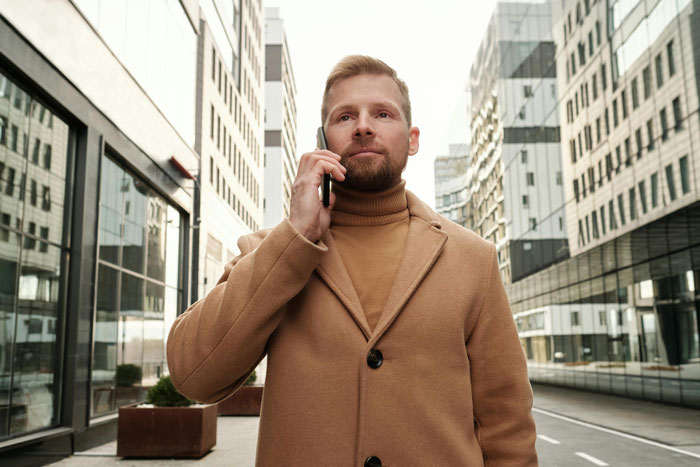 Man in tan coat talking on phone while standing on a city street, focused on an emotional conversation. Man in tan coat talking on phone while standing on a city street, focused on an emotional conversation.