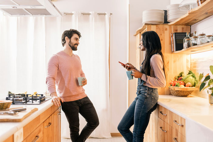 Man and sister-in-law talking in a cozy kitchen, both holding mugs, with fruit and spices on the counter. Man and sister-in-law talking in a cozy kitchen, both holding mugs, with fruit and spices on the counter.