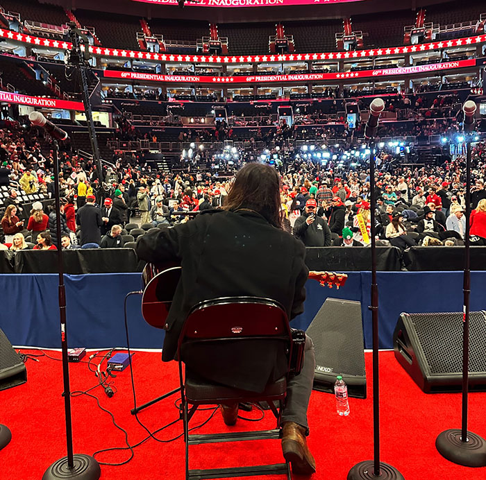 Musician at inauguration, viewed from behind on stage, with crowd and bright lights in auditorium. Musician at inauguration, viewed from behind on stage, with crowd and bright lights in auditorium.