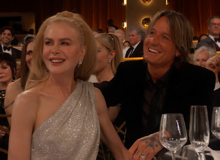 Nicole Kidman in a silver dress at a formal event, sitting with husband Keith Urban, amid other attendees. Nicole Kidman in a silver dress at a formal event, sitting with husband Keith Urban, amid other attendees.