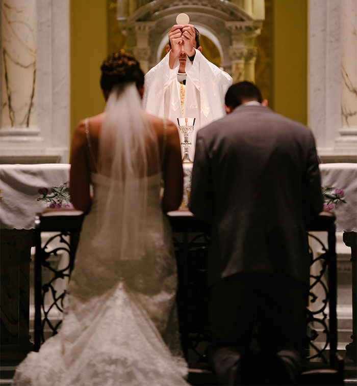 A bride and groom kneeling at the altar during a wedding ceremony, with a priest holding a host. A bride and groom kneeling at the altar during a wedding ceremony, with a priest holding a host.