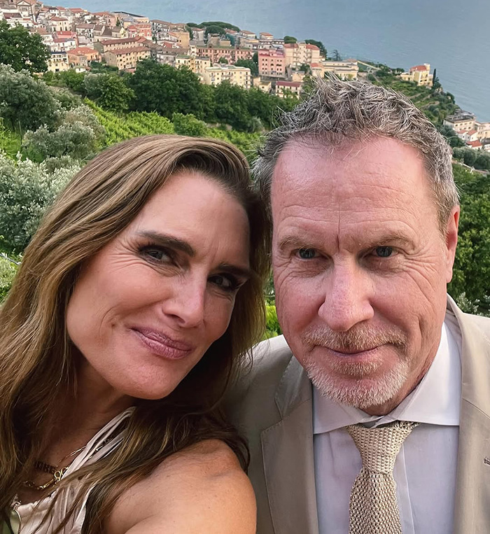 Brooke Shields with her husband smiling together in a scenic outdoor setting, overlooking a hillside town and the sea. Brooke Shields with her husband smiling together in a scenic outdoor setting, overlooking a hillside town and the sea.
