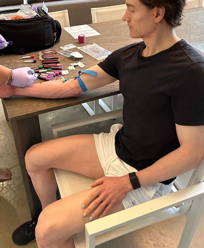 Bryan Johnson in black shirt and white shorts receiving a medical treatment related to longevity. Bryan Johnson in black shirt and white shorts receiving a medical treatment related to longevity.