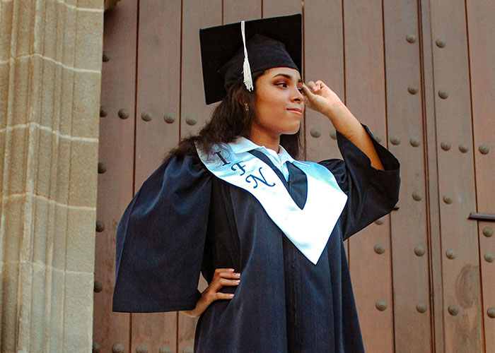 Young graduate in cap and gown, standing confidently in front of a wooden door, symbolizing university achievement. Young graduate in cap and gown, standing confidently in front of a wooden door, symbolizing university achievement.
