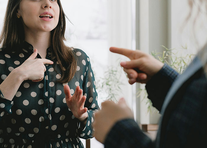 People in discussion, one wearing polka dots, gesturing while talking about university importance. People in discussion, one wearing polka dots, gesturing while talking about university importance.