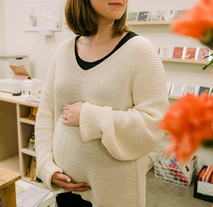 Pregnant retail worker in a cozy shop setting, wearing a cream sweater, representing retail workers' unique experiences.