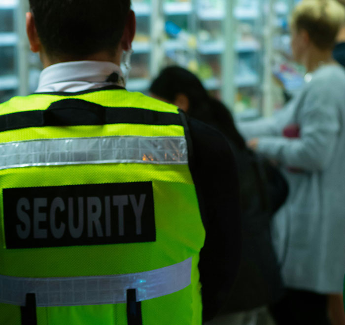 Security guard in a bustling retail store, wearing a yellow vest.
