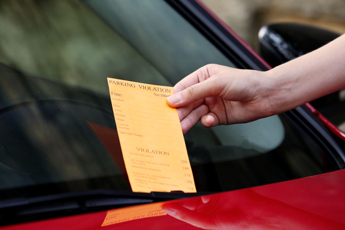 A parking ticket placed on a red car's windshield in a driveway block scenario. A parking ticket placed on a red car's windshield in a driveway block scenario.