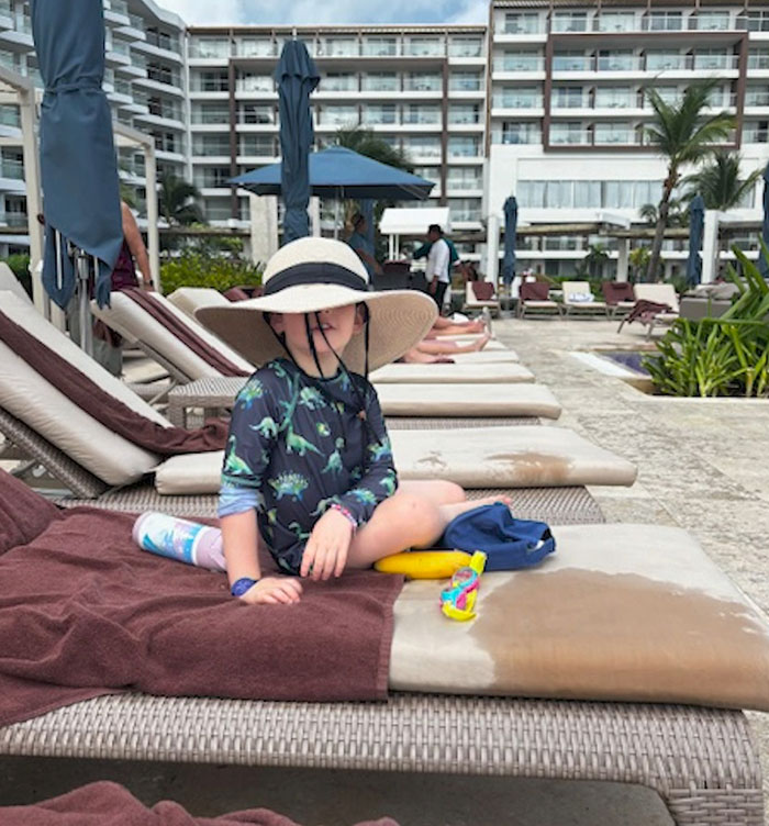 Child in a sun hat on resort lounge chair by poolside in Cancun, surrounded by vacationers. Child in a sun hat on resort lounge chair by poolside in Cancun, surrounded by vacationers.
