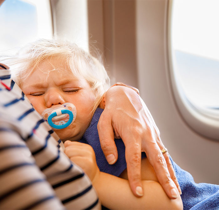 Crying child with pacifier being comforted on airplane, related to seat swap incident. Crying child with pacifier being comforted on airplane, related to seat swap incident.