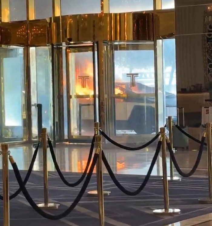Cybertruck surrounded by flames in a building entrance, reflecting off golden glass doors. Cybertruck surrounded by flames in a building entrance, reflecting off golden glass doors.