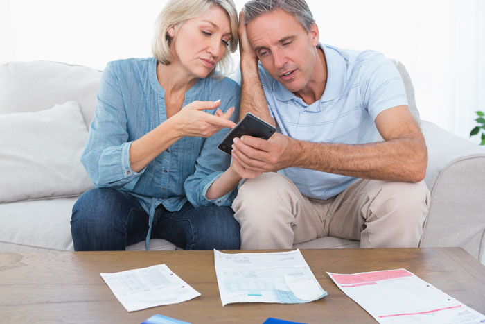 Parents looking stressed, sitting on a couch, surrounded by financial documents and reviewing a phone together. Parents looking stressed, sitting on a couch, surrounded by financial documents and reviewing a phone together.