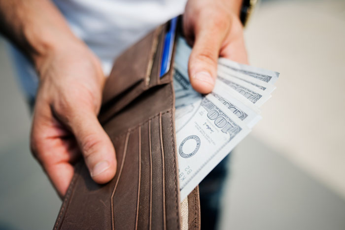 Person holding a wallet with cash, highlighting disparity in financial management and family college fund allocation. Person holding a wallet with cash, highlighting disparity in financial management and family college fund allocation.