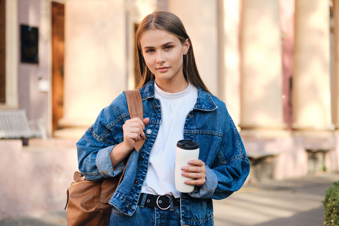 Young woman in denim jacket, holding a cup, symbolizes struggles with college costs compared to lavish sibling lifestyle. Young woman in denim jacket, holding a cup, symbolizes struggles with college costs compared to lavish sibling lifestyle.