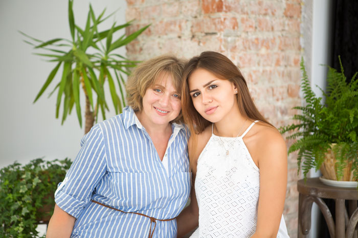 Two women posing together indoors, surrounded by plants, expressing contentment and family bond. Two women posing together indoors, surrounded by plants, expressing contentment and family bond.