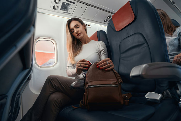 Woman seated on plane, holding a bag, exemplifying airline compassion and urgency to reach her terminally ill mother. Woman seated on plane, holding a bag, exemplifying airline compassion and urgency to reach her terminally ill mother.