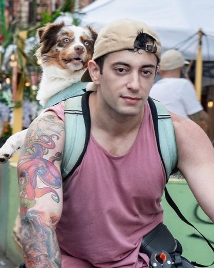 Tattooed man with NYC dog in backpack, both gazing ahead in a lively street scene. Tattooed man with NYC dog in backpack, both gazing ahead in a lively street scene.