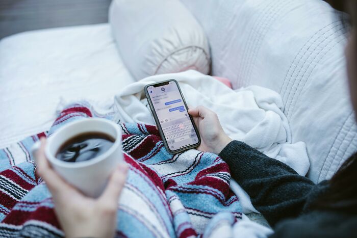 A woman holding a smartphone, texting, while sipping coffee on a cozy couch. A woman holding a smartphone, texting, while sipping coffee on a cozy couch.