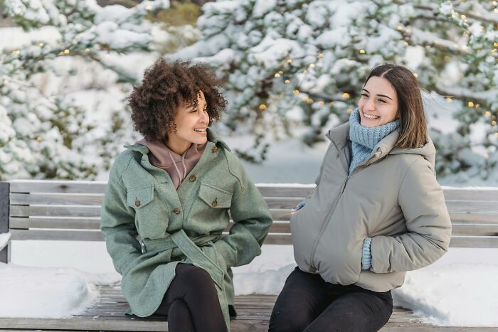 Two women in winter coats chatting on a snowy bench, symbolizing friendship and connection. Two women in winter coats chatting on a snowy bench, symbolizing friendship and connection.