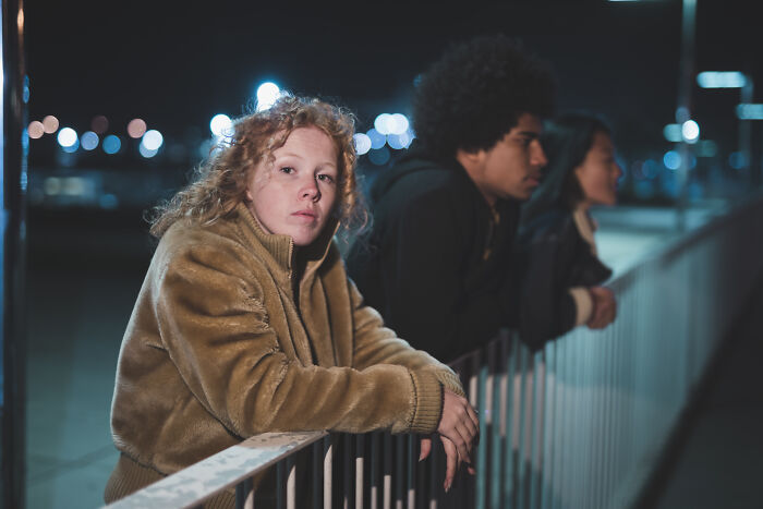 Three people leaning on a railing at night, one looking at the camera, representing friendship and distance over time. Three people leaning on a railing at night, one looking at the camera, representing friendship and distance over time.