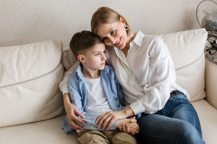 Teen sitting on a couch, looking thoughtful, next to a woman who has her arm around him. Teen sitting on a couch, looking thoughtful, next to a woman who has her arm around him.