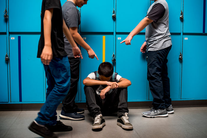 Teen enduring bullying, sitting by lockers, surrounded by peers pointing. Teen enduring bullying, sitting by lockers, surrounded by peers pointing.