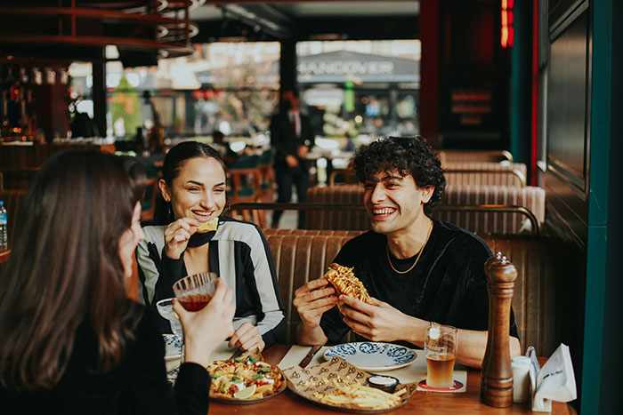 Three friends dining joyfully in a restaurant, sharing a meal and drinks, embodying friendship and lively conversation. Three friends dining joyfully in a restaurant, sharing a meal and drinks, embodying friendship and lively conversation.