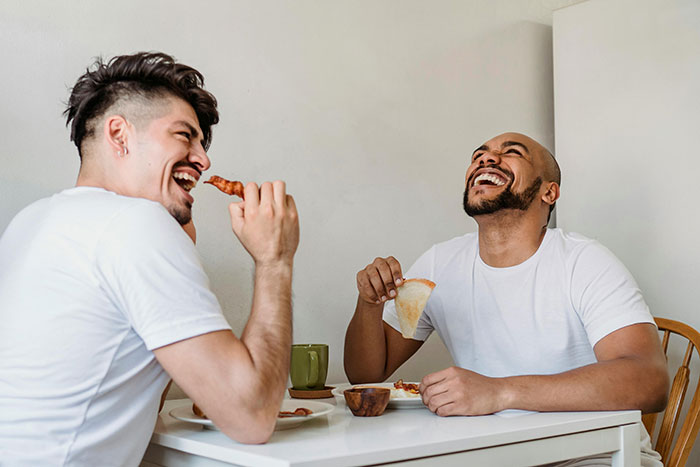 Two friends laughing while eating a home-cooked meal at a dining table. Two friends laughing while eating a home-cooked meal at a dining table.