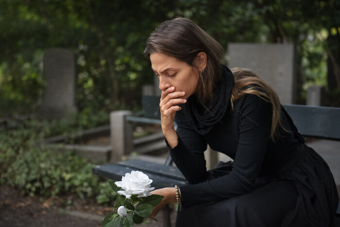 Woman in a cemetery holding a white rose, mourning a dead partner. Woman in a cemetery holding a white rose, mourning a dead partner.