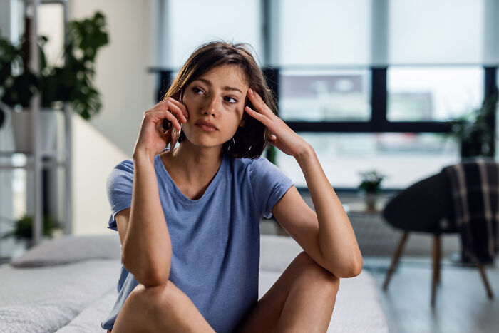 Woman on bed with thoughtful expression, arm to head, relating to friend and partner topics. Woman on bed with thoughtful expression, arm to head, relating to friend and partner topics.