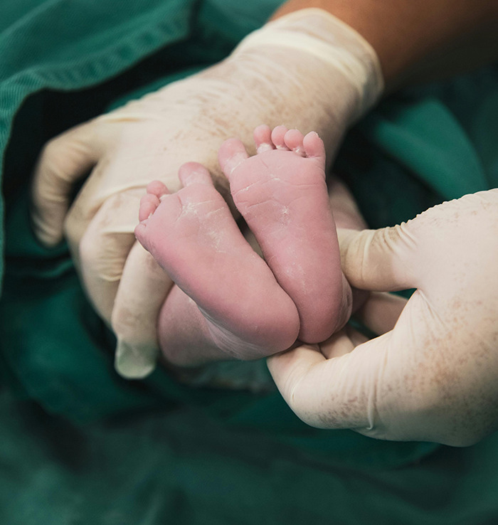 Newborn feet held by gloved hands in a hospital setting. Newborn feet held by gloved hands in a hospital setting.